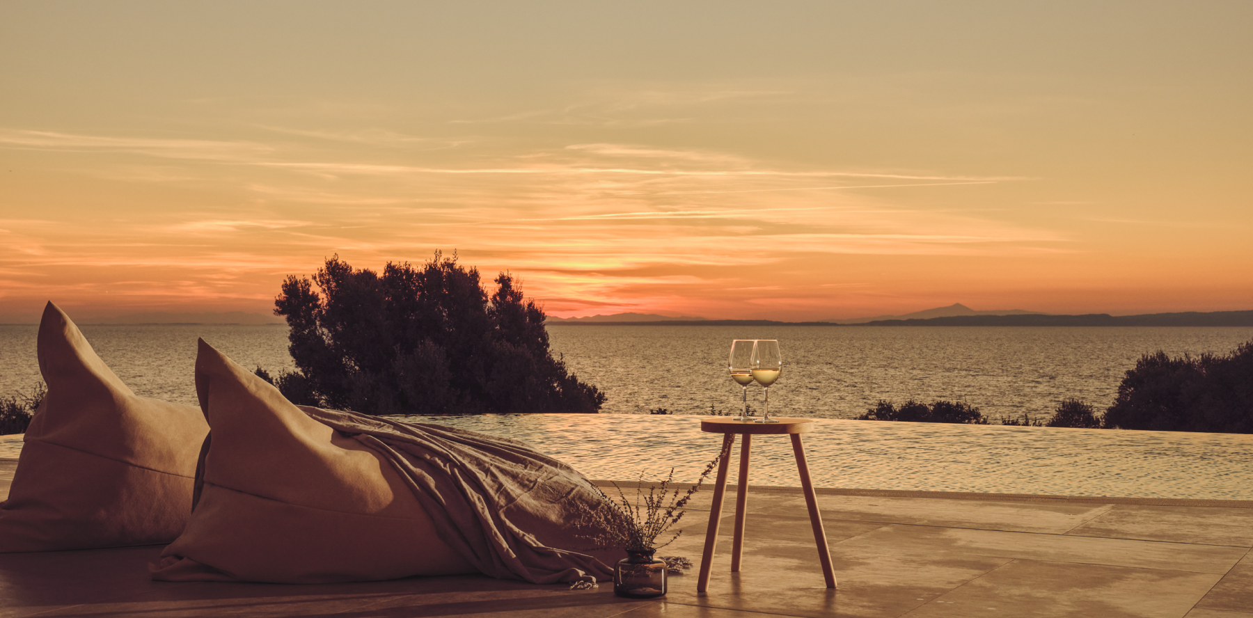 A glass of wine on a chair by the ocean at sunset, creating a serene and relaxing ambiance.